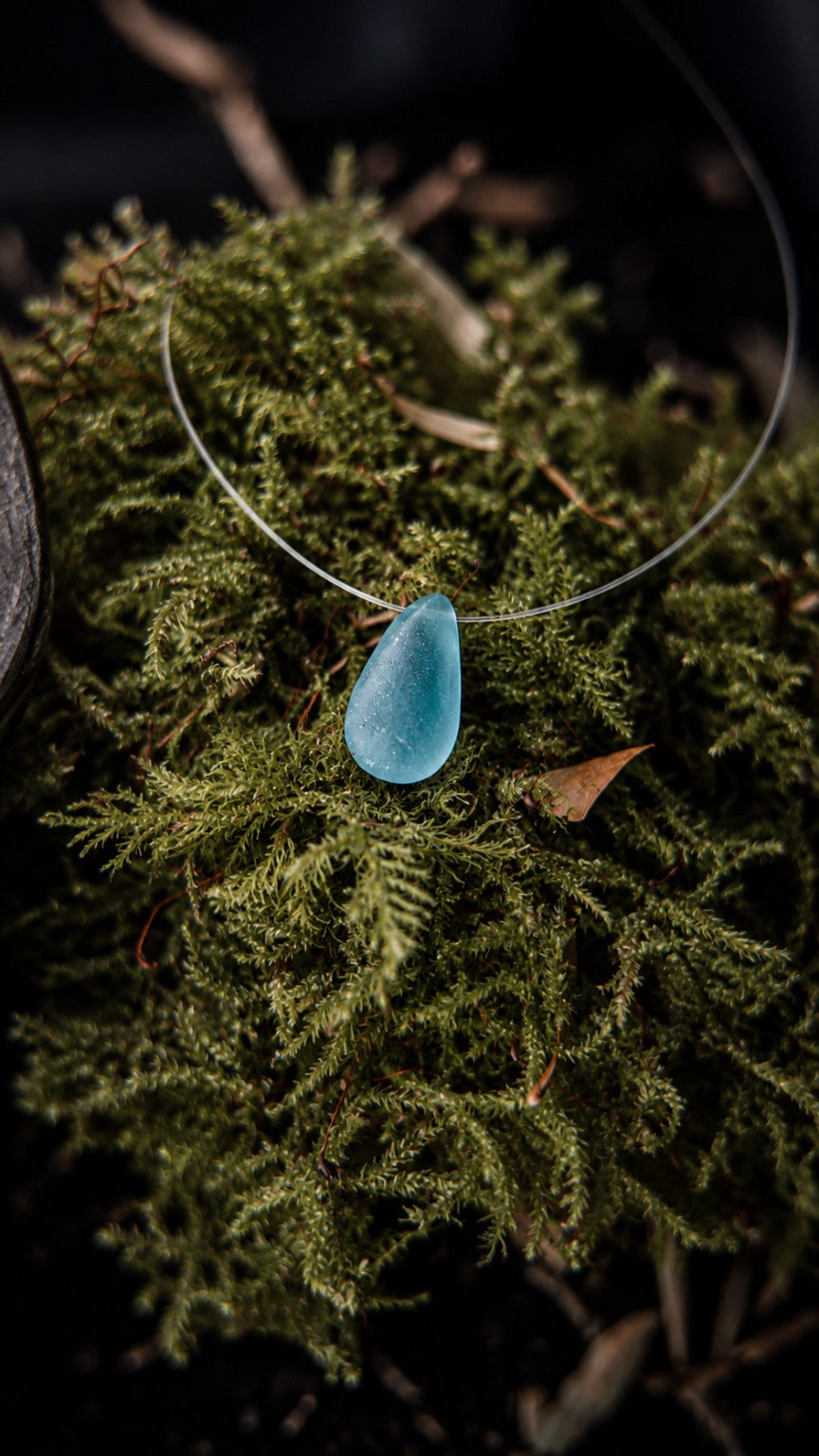 Néréide, collier Olibria sur fil transparent avec pendentif en verre de mer bleu retaillé à la main, photographié sur de la mousse.