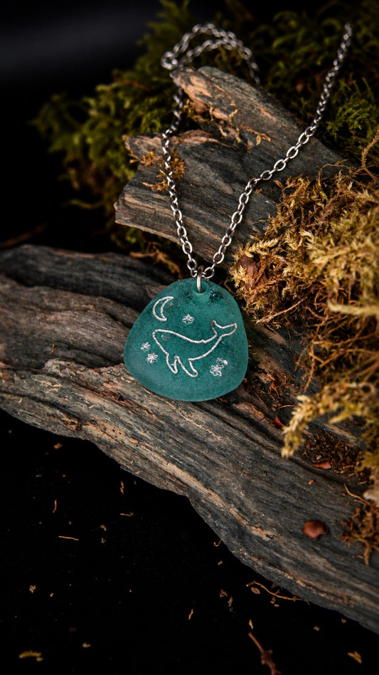 Cetya, collier Olibria en verre bleu recyclé fondu à l’atelier, gravé d’une baleine, d’une lune et d’étoiles, sur chaîne en acier inoxydable argenté.